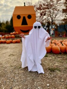 Child in Ghost Costume in Front of Pumpkins